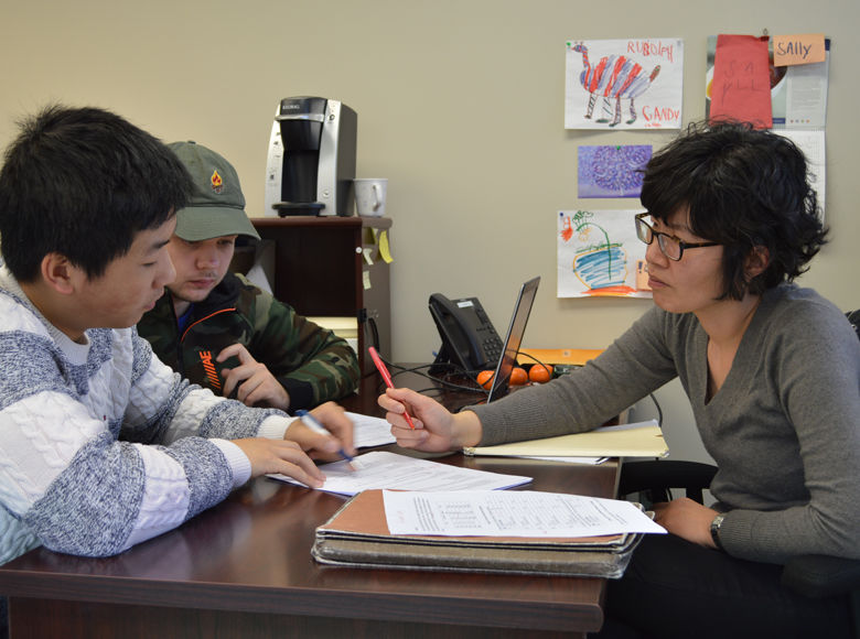 two students sitting at desk talking to staff member