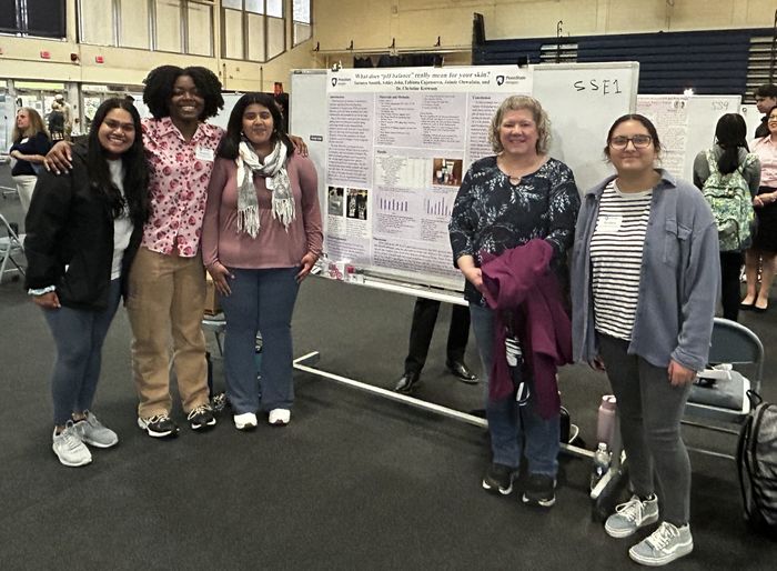 students and Chris standing in front of poster at ACURA fair