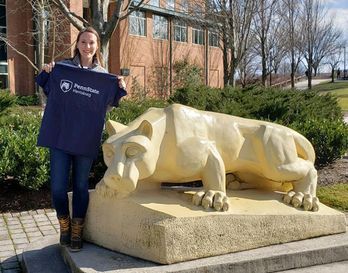 Kailee Shotto stands next to the Harrisburg Lion Shrine and holds up a Penn State Harrisburg tee shirt.