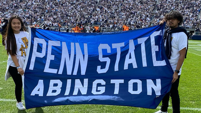 two students at Beaver Stadium with Penn State Abington banner