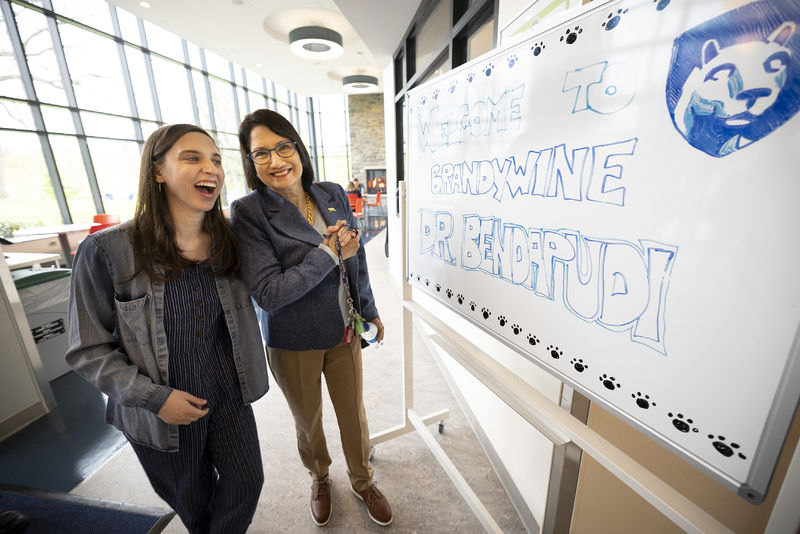 Two women stand next to a white board with a welcome message.