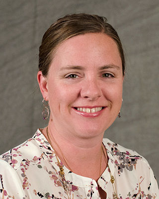 photo portrait of woman with brown hair swept back and wearing cream colored floral blouse