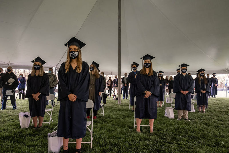 Graduates in caps and gowns standing under large white tent.