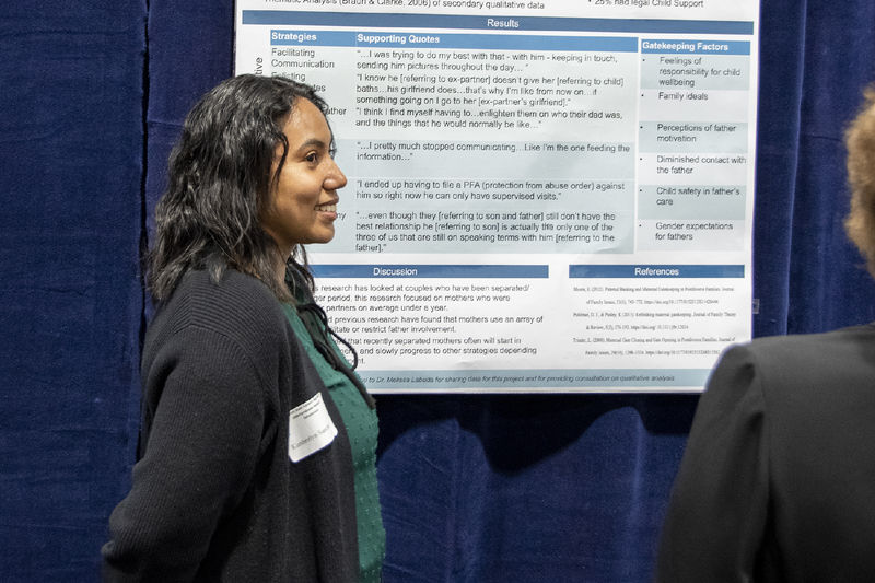 Girl with dark curly hair wearing a black cardigan presents research poster