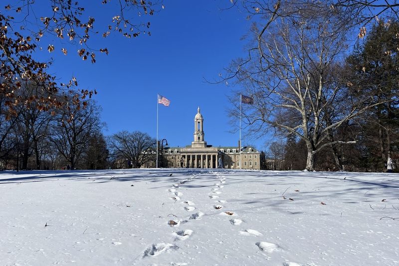 A faraway picture of Old Main with a blue sky behind it and several paths of footprints in the snow leading to it