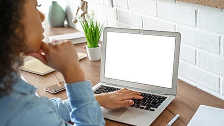 A female student wearing a blue shirt is pictured working at a laptop.