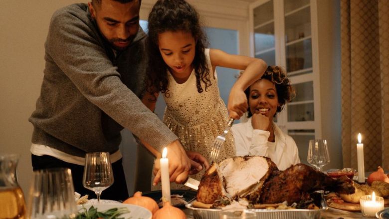 Father, child, mother carve a turkey at Thanksgiving