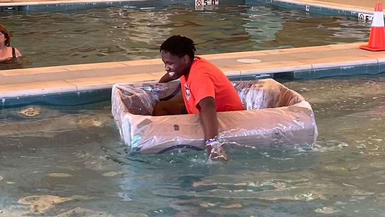 Student paddling cardboard boat in a pool.