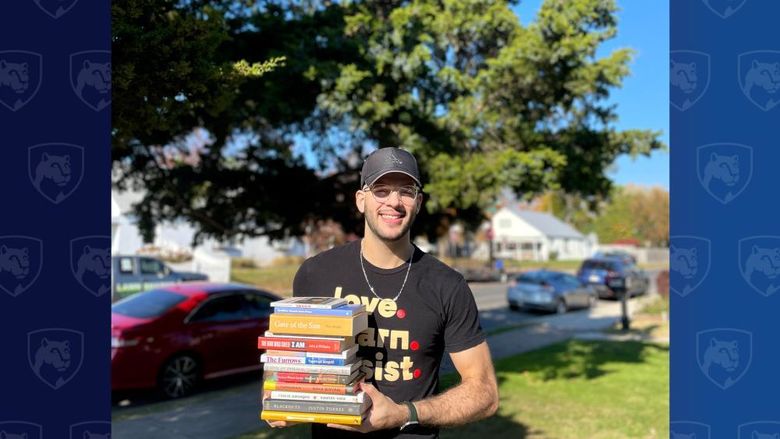 Man holding stack of books in front of a tree