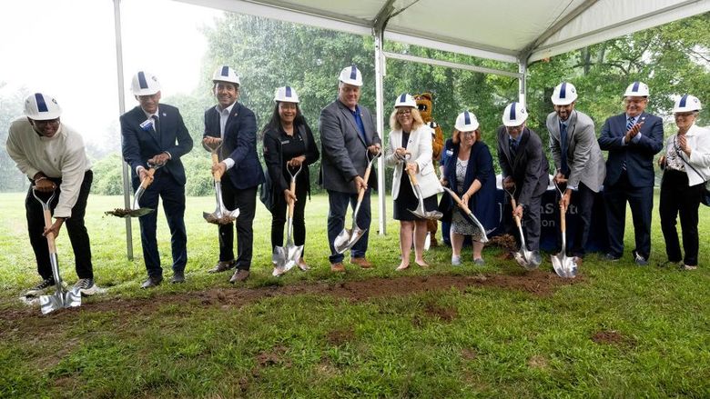 People shoveling dirt under a tent to break ground for new construction