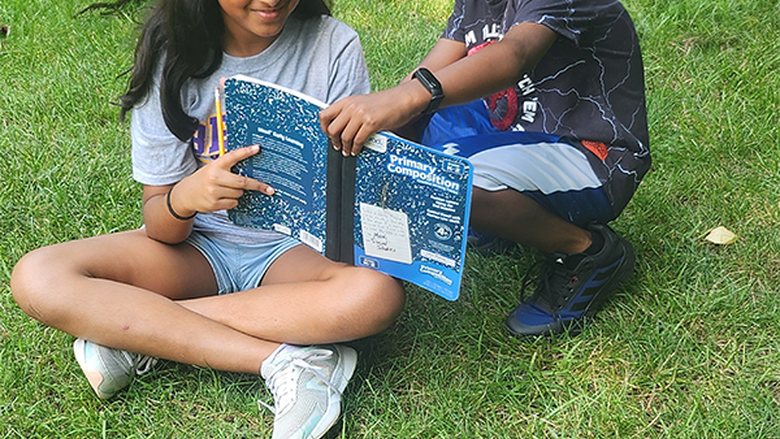 two students sitting in the grass reading
