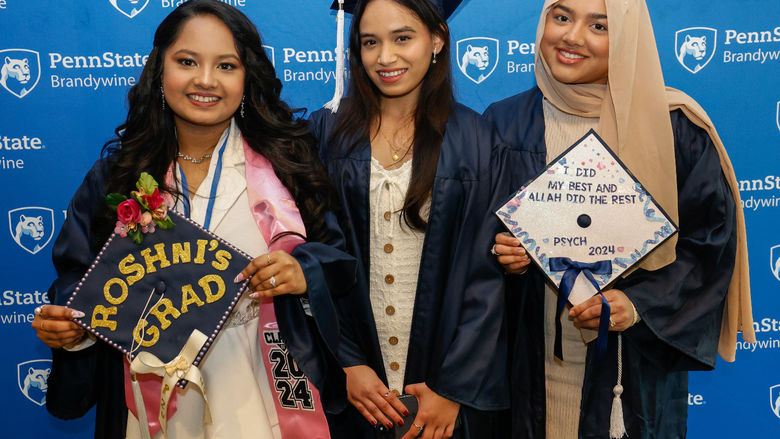 Three female students pose for a photo wearing their commencement gowns.