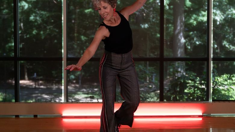 Woman tap dancing in a studio in front of wall of windows