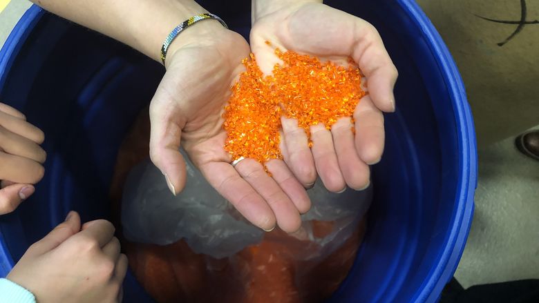 hands hold orange plastic particles