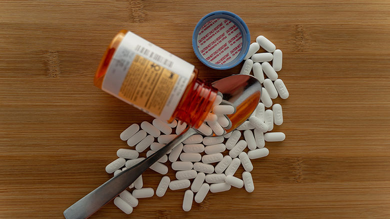 Prescription pills spilled out of the bottle onto a wooden table with a spoon