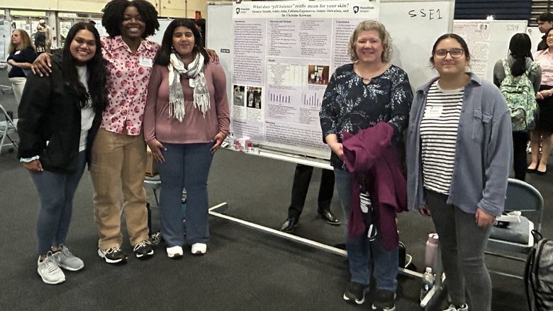 students and Chris standing in front of poster at ACURA fair