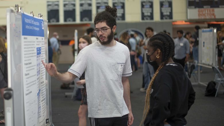 Student talking about his poster project to another student at ACURA fair