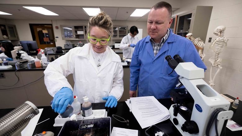 student in lab coat working with their professor