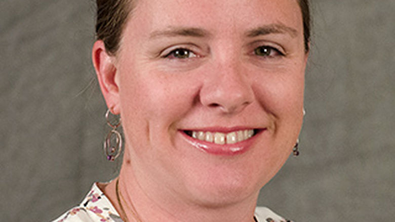 photo portrait of woman with brown hair swept back and wearing cream colored floral blouse