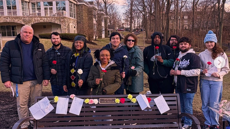 People standing around memorial bench with flowers