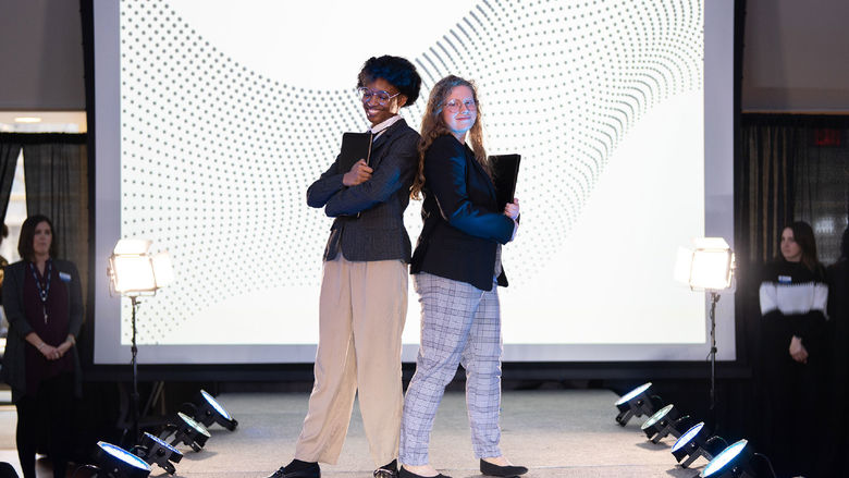 Two students pose on a runway at a fashion show