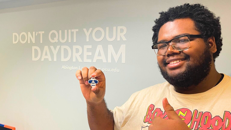 Darryl Gregory holds up a 3D print of a bee in front of a wall that says "Don't quit your daydream."