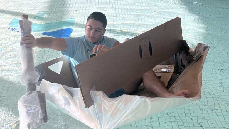 Student paddling cardboard boat in a pool