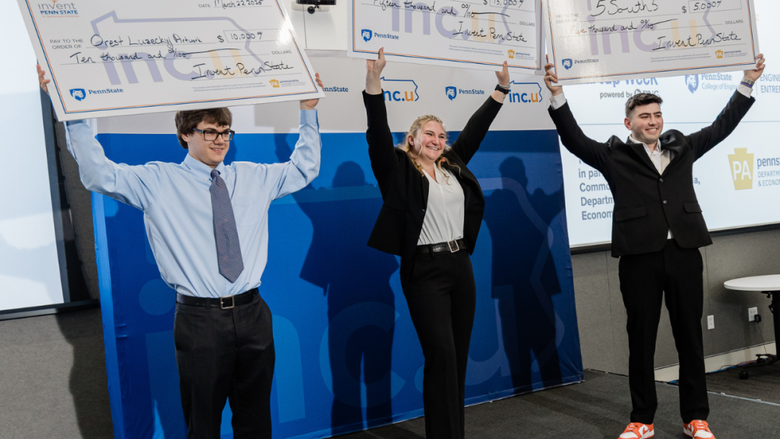 Three individuals stand on a stage holding up oversized checks
