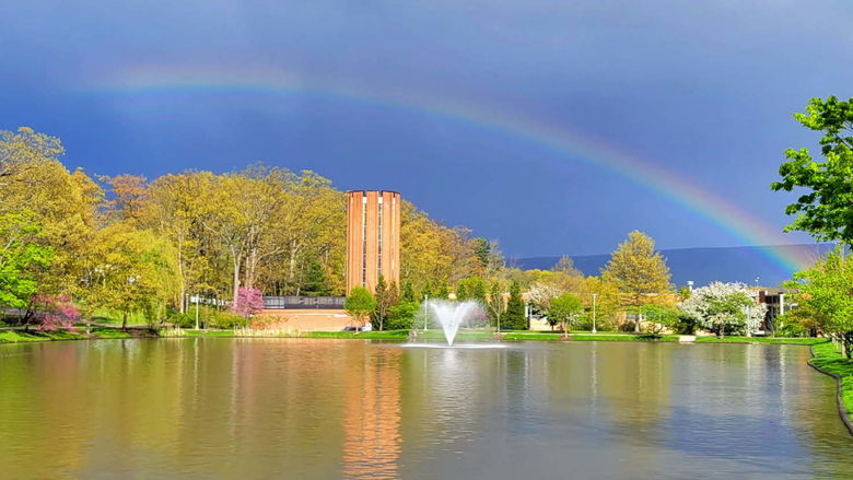 A rainbow against a dark sky over a pond on a college campus