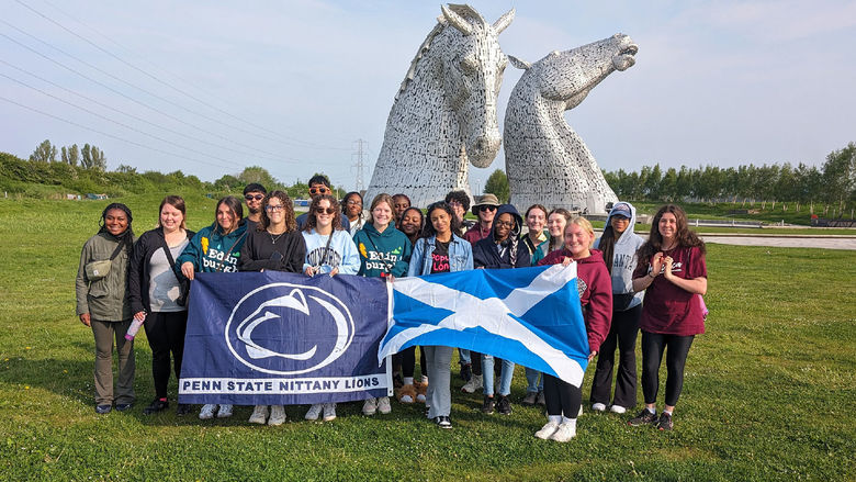 Students with a flag in front of twin horse statues