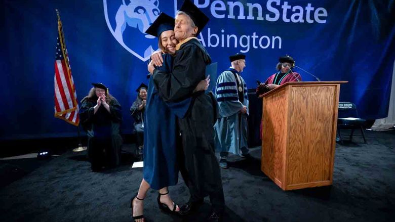 student and professor hugging on commencement stage