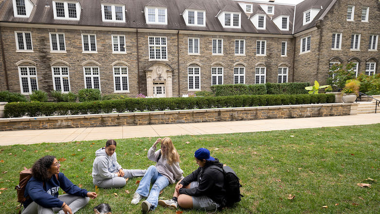 four students sitting on the grass in front of Sutherland building