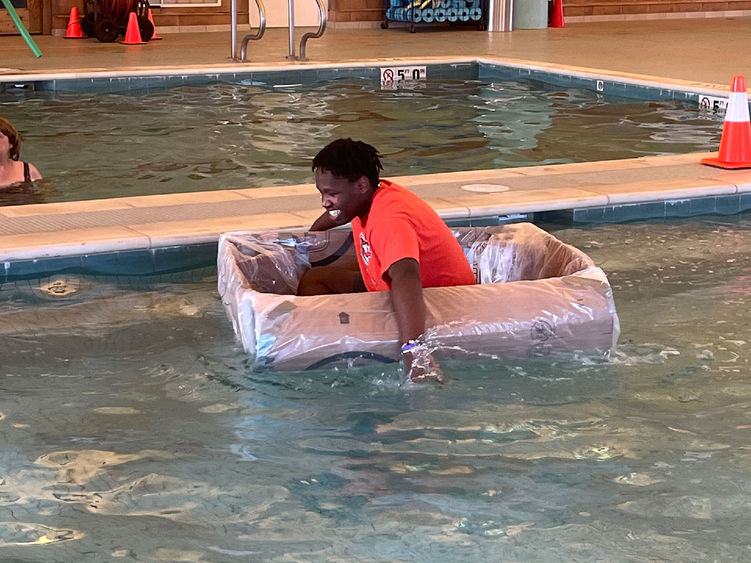 Student paddling cardboard boat in a pool.