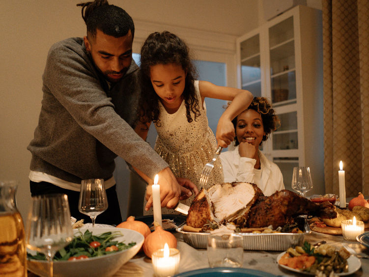 Father, child, mother carve a turkey at Thanksgiving