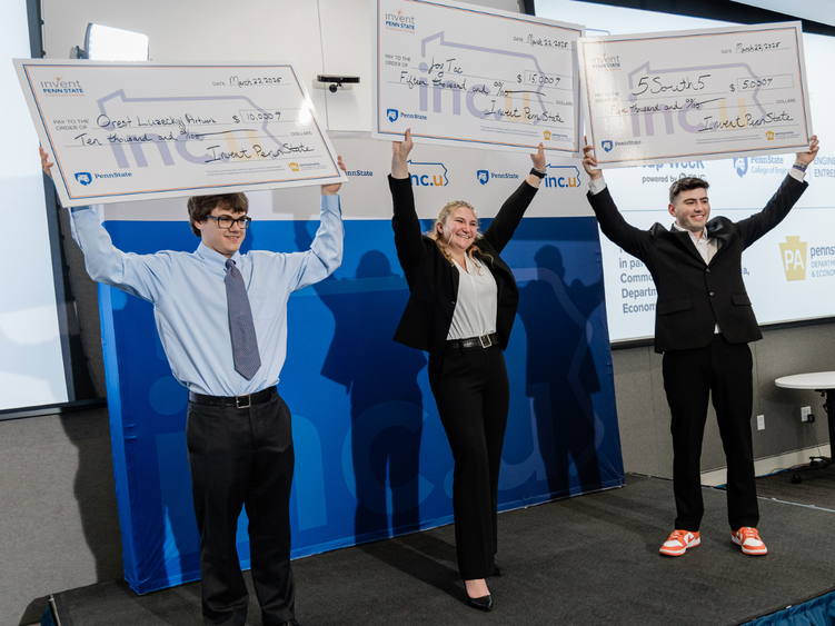 Three individuals stand on a stage holding up oversized checks