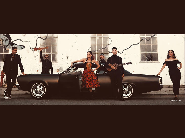 Members of a band hold instruments while standing around a black car